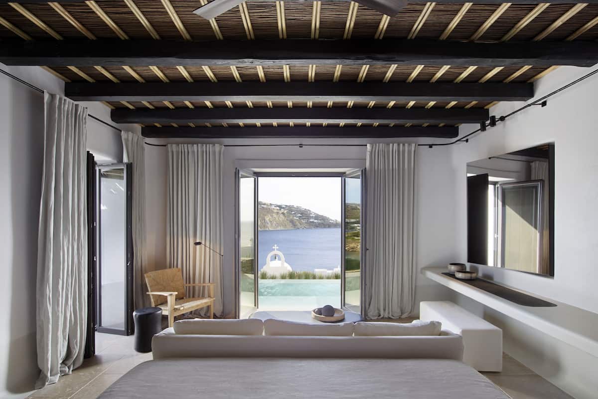 A bedroom with a large bed, a view of the sea, and a wooden ceiling.