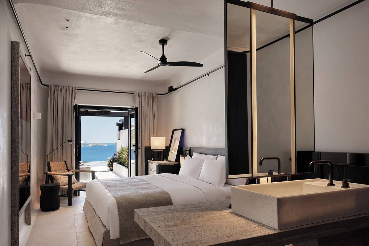 A modern hotel room with a large bed, a built-in vanity, and a view of the sea.
