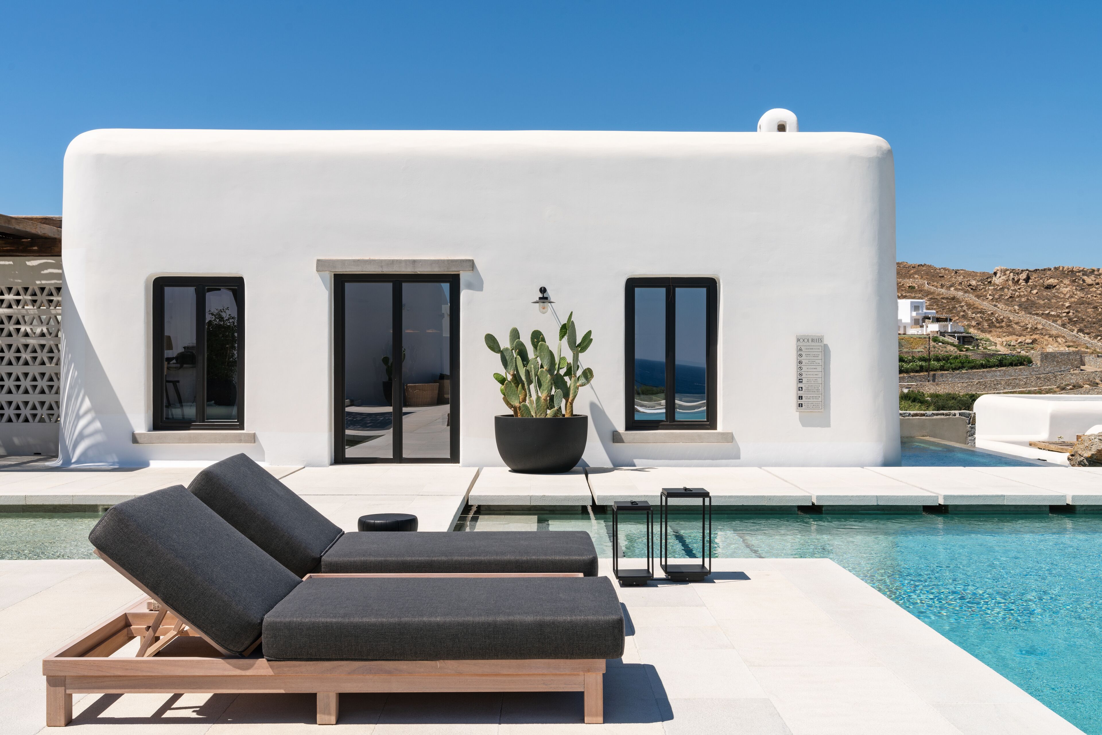 A modern building with a pool, two lounge chairs, and a potted plant.