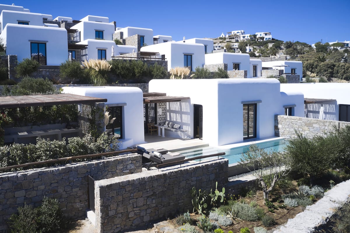 A coastal building with white walls and stone accents, featuring a pool and outdoor seating.