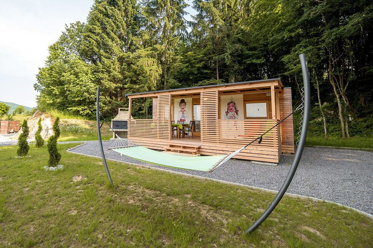 Une cabane en bois avec un porche, entourée d’arbres.