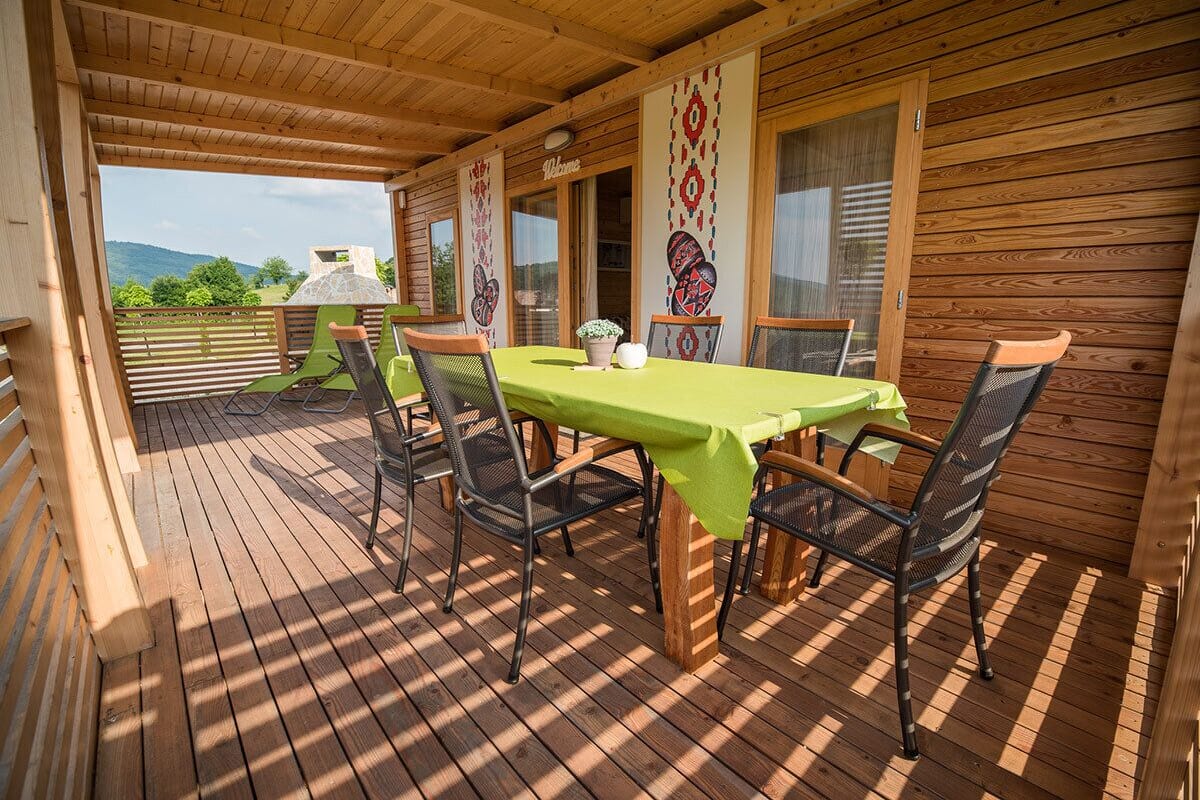 Une terrasse en bois avec une table et des chaises, une vue sur les montagnes et une pancarte indiquant « Bienvenue ».