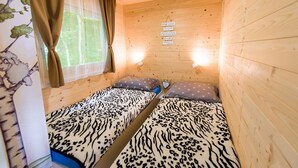 Een gezellige kamer met houten wanden en twee bedden met luipaardprint beddengoed. Er zijn twee wandlampen en een raam met gordijnen.