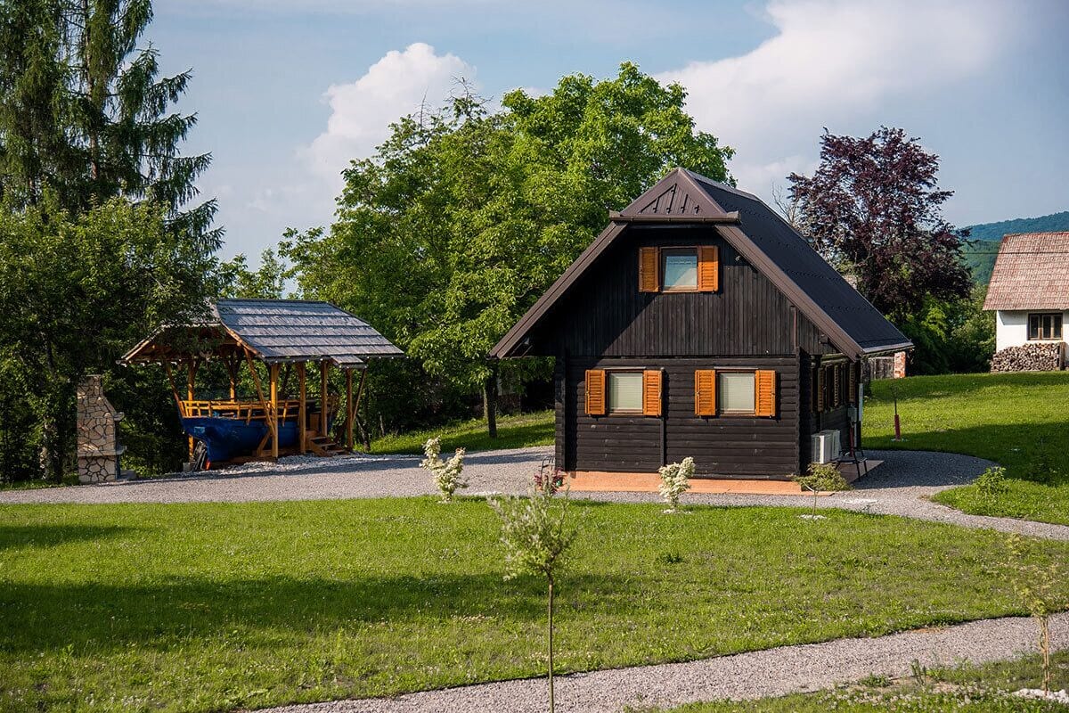 Une cabane en bois avec un toit en pente, un petit porche et une construction en pierre à proximité.