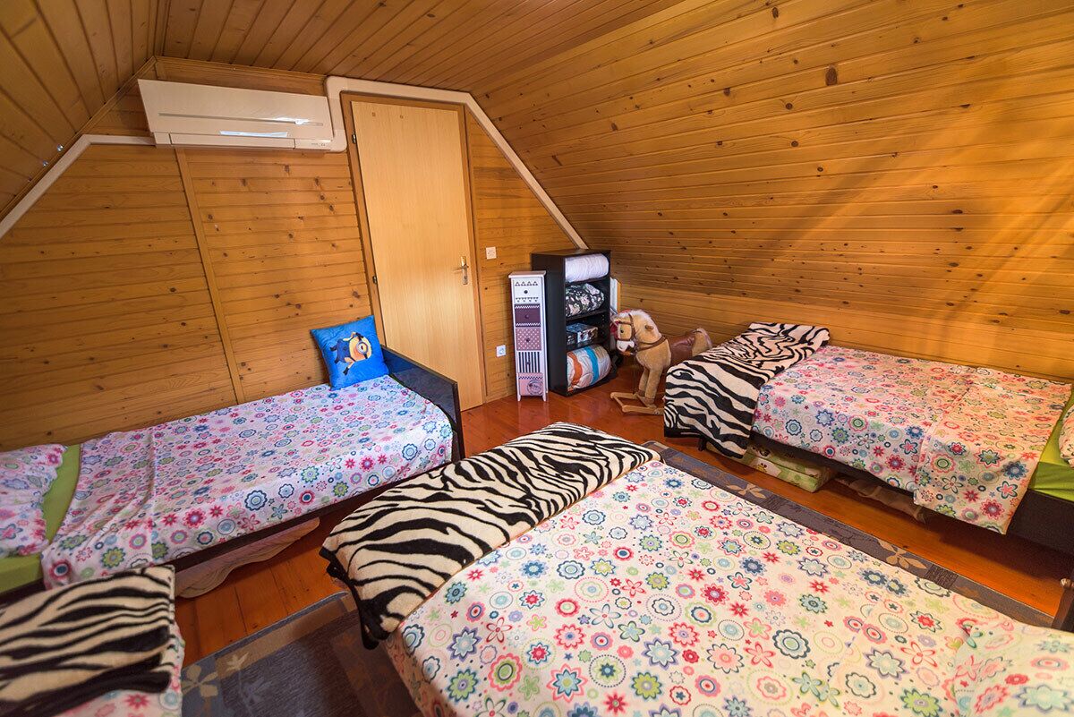 Un dormitorio acogedor en el ático con tres camas, techo inclinado de madera y un pequeño espacio de almacenamiento.