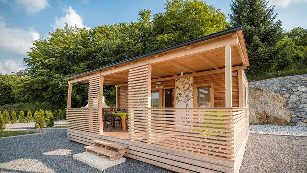 Een houten blokhut met een overdekte veranda, een stenen muur en een grindpad.