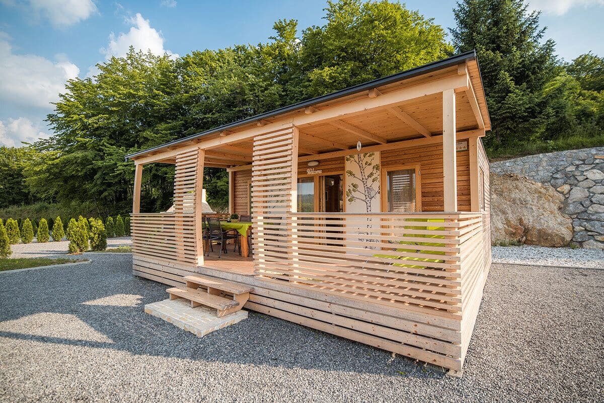 Une cabane en bois avec un porche couvert, un mur en pierre et une allée gravillonnée.