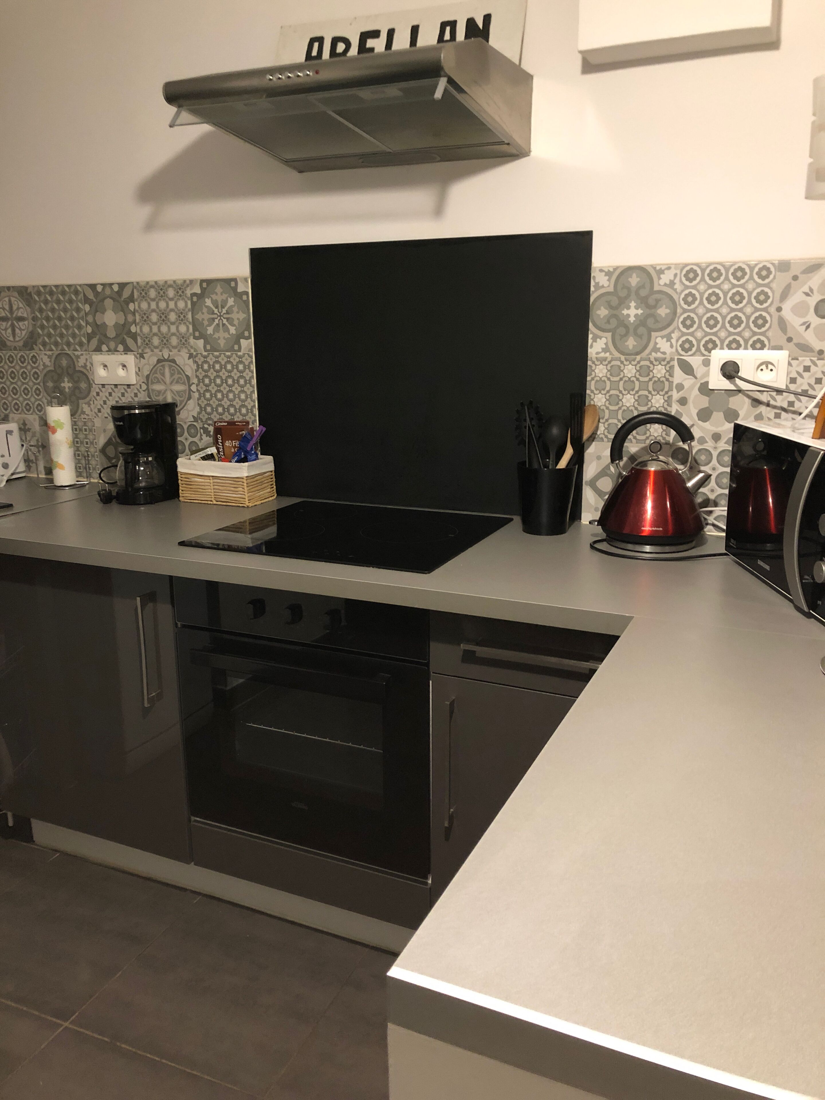 A modern kitchen with a black stove, a red kettle, and a coffee maker.