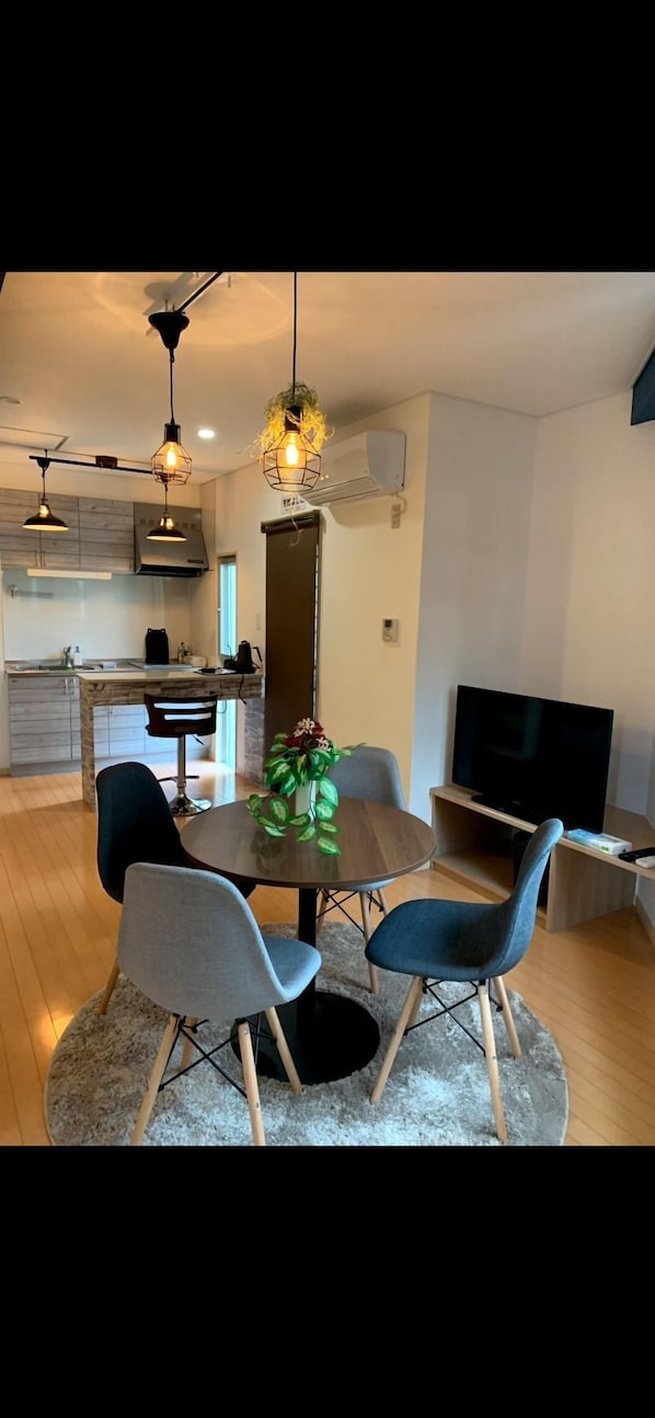 Una cocina moderna con iluminación colgante, una mesa de comedor con sillas, un televisor y una planta.