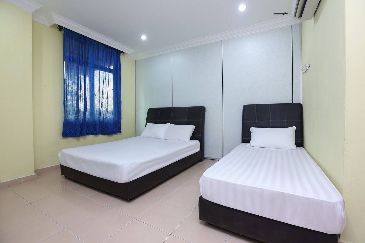 Two single beds with white linens in a room with beige walls and a blue curtain.