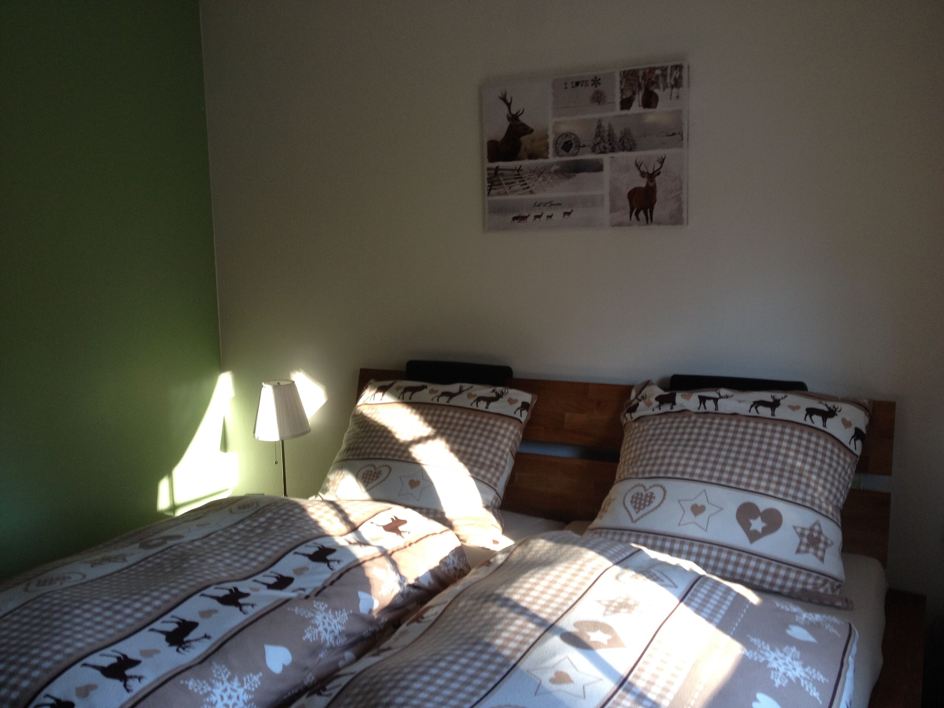 A bedroom with a bed featuring checkered bedding with animal prints, a wall-mounted artwork with nature and wildlife images, and a lamp on the left side.