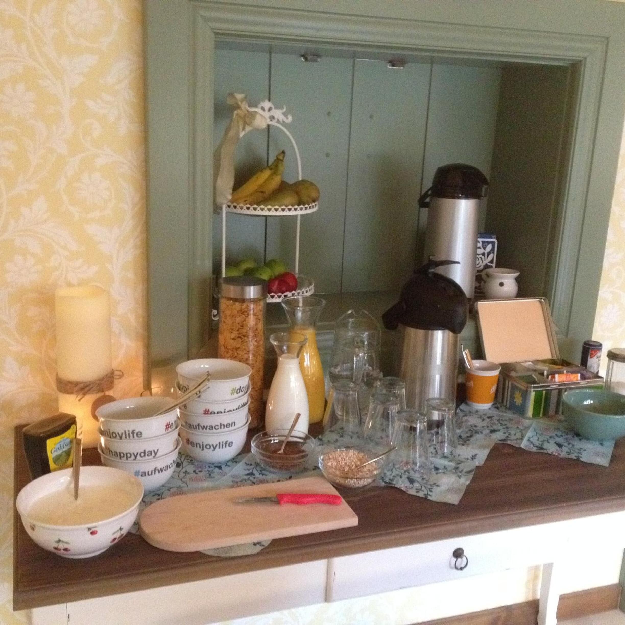 Un plan de travail de cuisine sur lequel on trouve divers objets, notamment un panier de fruits, un thermos, une machine à café, ainsi que plusieurs bols et bocaux.