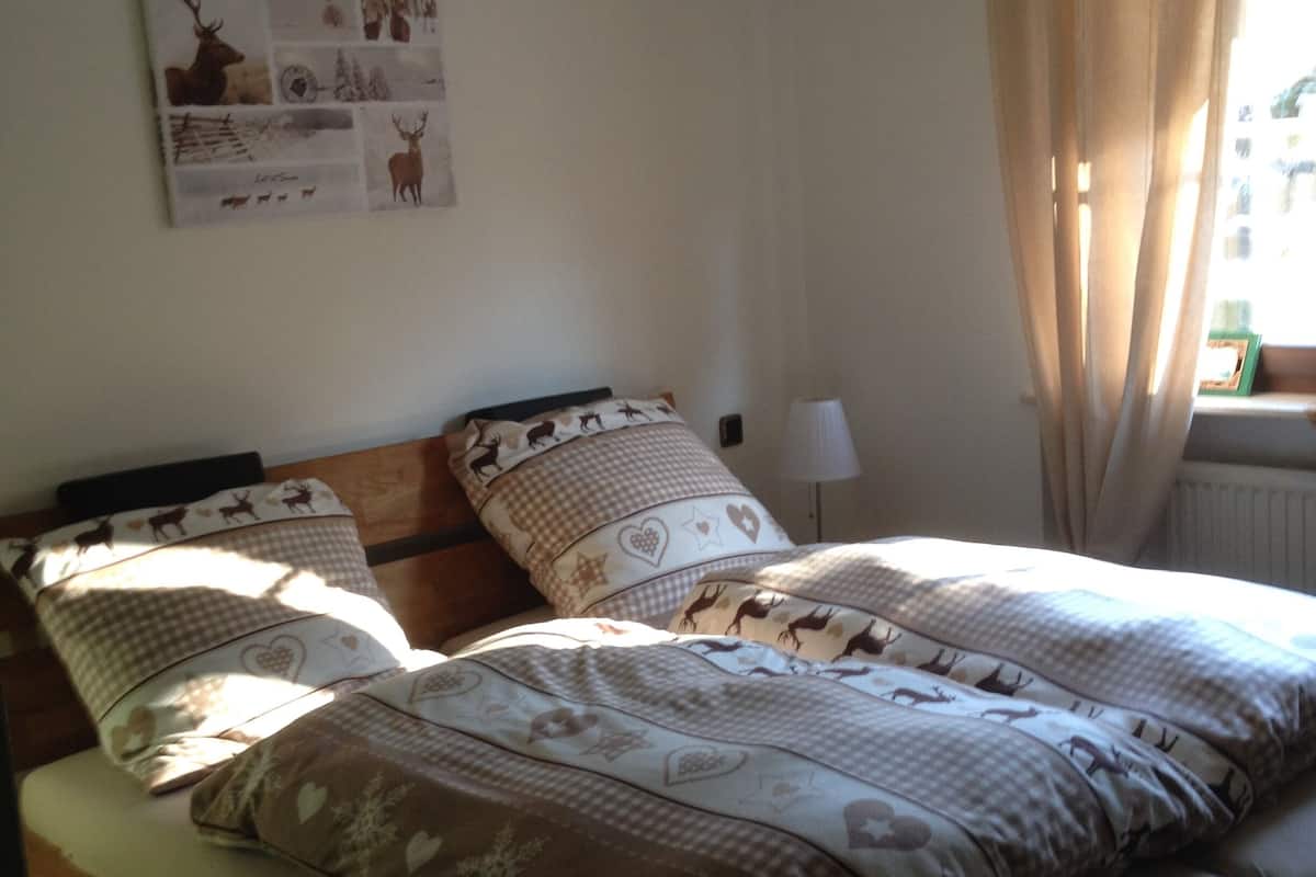 A bed with a checkered and heart-patterned duvet, a headboard, and a wall-mounted picture of deer.