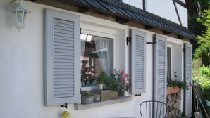A white building with shutters, a small window with plants, a yellow lantern, and two metal chairs. - Ferienhaus Romantikmühle Heartlandranch (Horbruch)