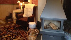 A cozy room with a fireplace, a chair with a white throw, a wooden floor, and a patterned rug. - Ferienhaus Romantikmühle Heartlandranch (Horbruch)