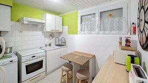 Une cuisine compacte avec des meubles blancs, un four encastré, un évier et un petit coin repas équipé de tabourets.
