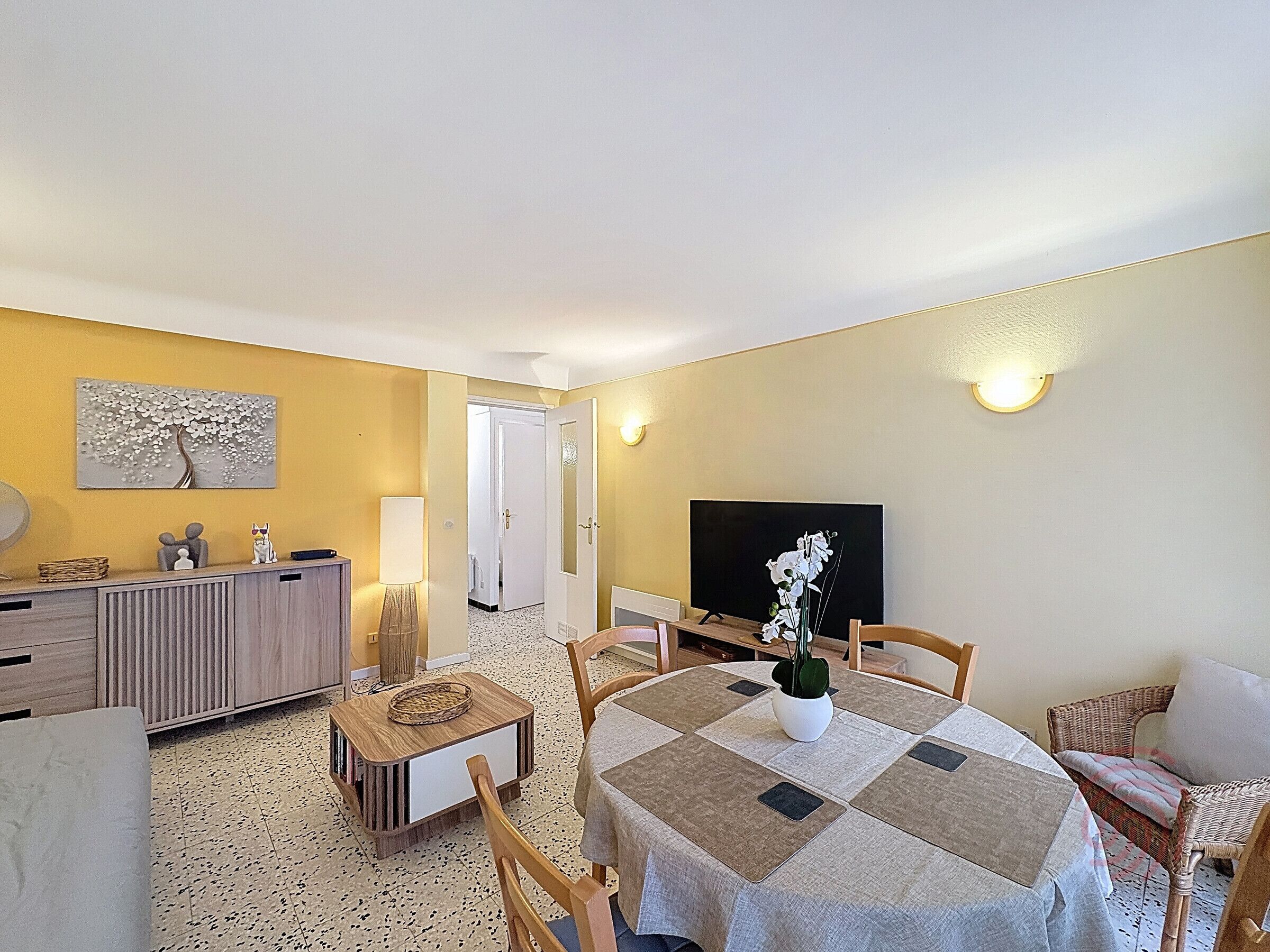 A living room with a dining area, a TV, and a door leading to another room.