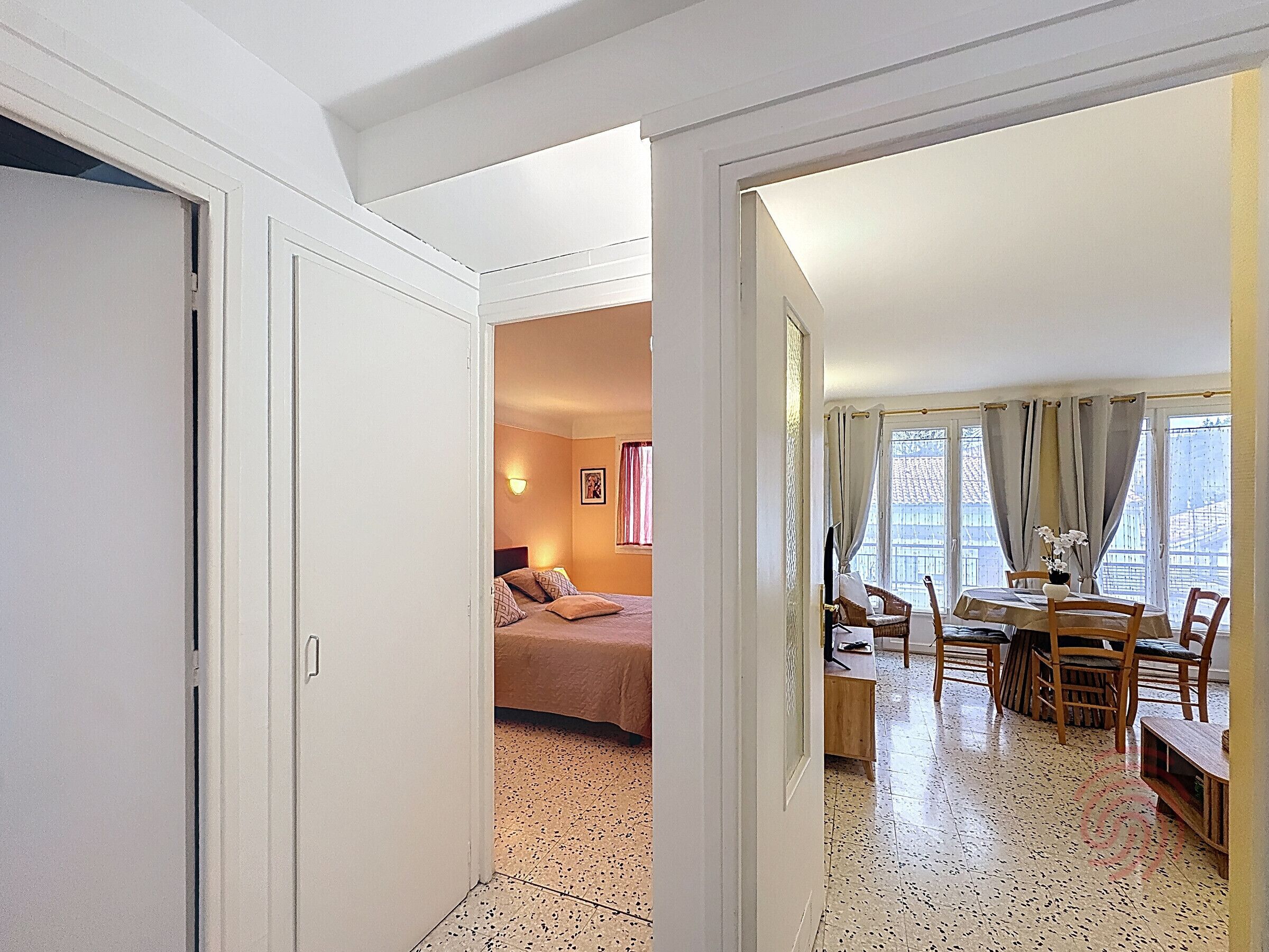 A hotel room with a bed, a dining area with a table and chairs, and a view of the outside through large windows.