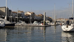 A marina with boats docked, a pier, and buildings in the background.