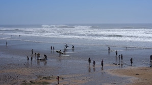 A beach with people, some carrying surfboards, and waves in the background.