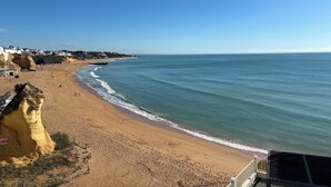 A beach with a rocky cliff, a clear sky, and a calm sea.