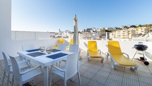 A rooftop terrace with a table and chairs, a grill, and a view of the city.