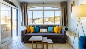 A modern living room with a large window, a sofa with colorful cushions, a small table, and a floor lamp.