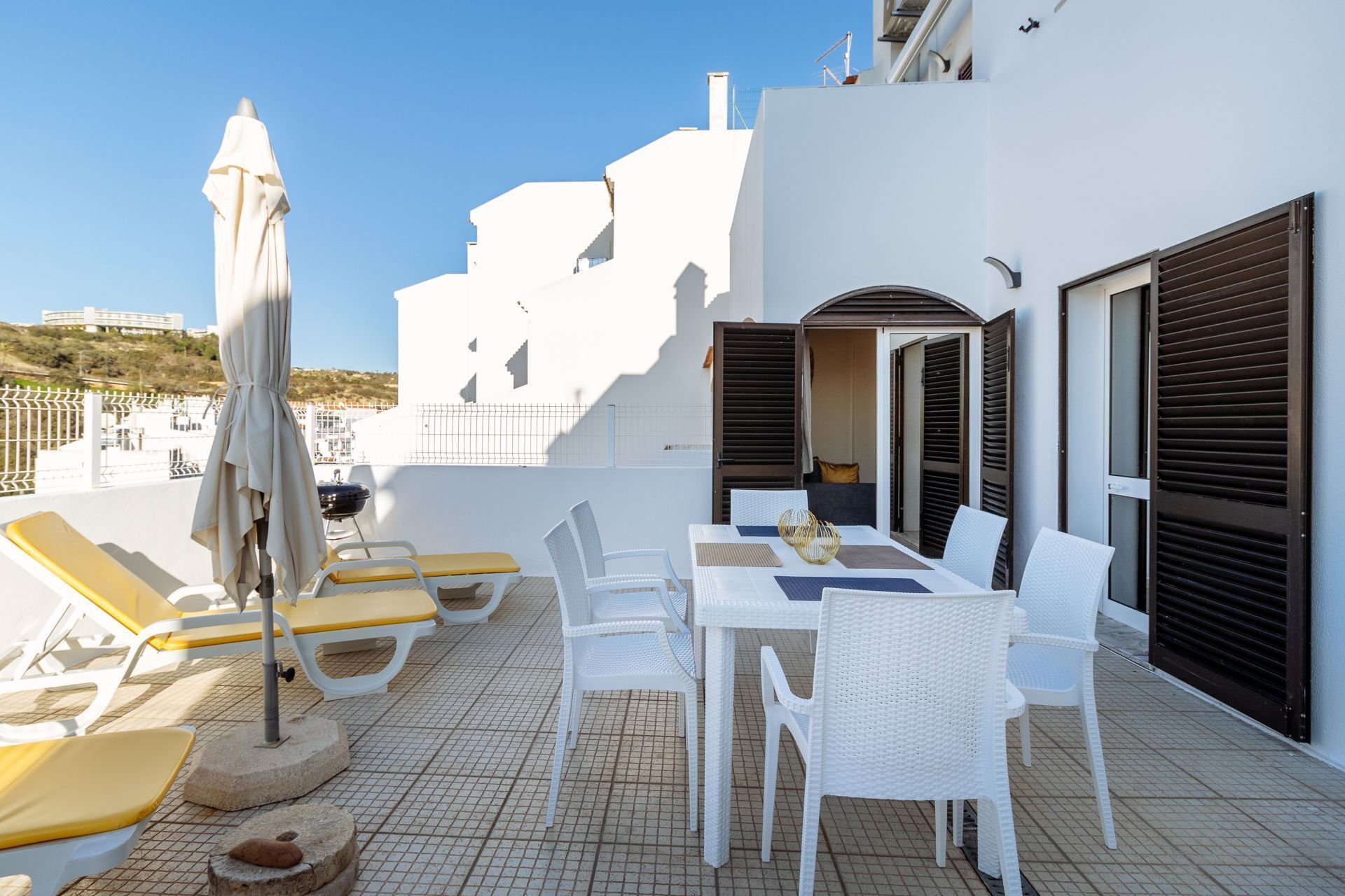 Terraza en la azotea con mobiliario blanco, que incluye una mesa y sillas, y una sombrilla.