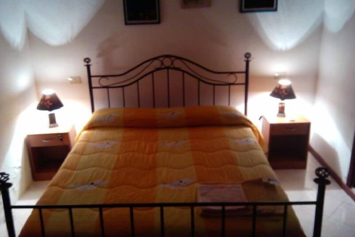Un lit simple avec un cadre en métal, deux tables de chevet avec des lampes et un tableau accroché au mur au-dessus du lit.