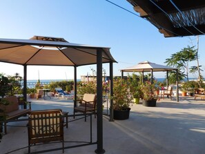 An outdoor patio area with seating arrangements, potted plants, and a view of the sea. - Case La Pergola (Santa Marina Salina)