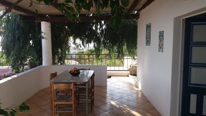 A covered patio with a table and chairs, a bowl of fruit, and a view of greenery and a fence. - Case La Pergola (Santa Marina Salina)