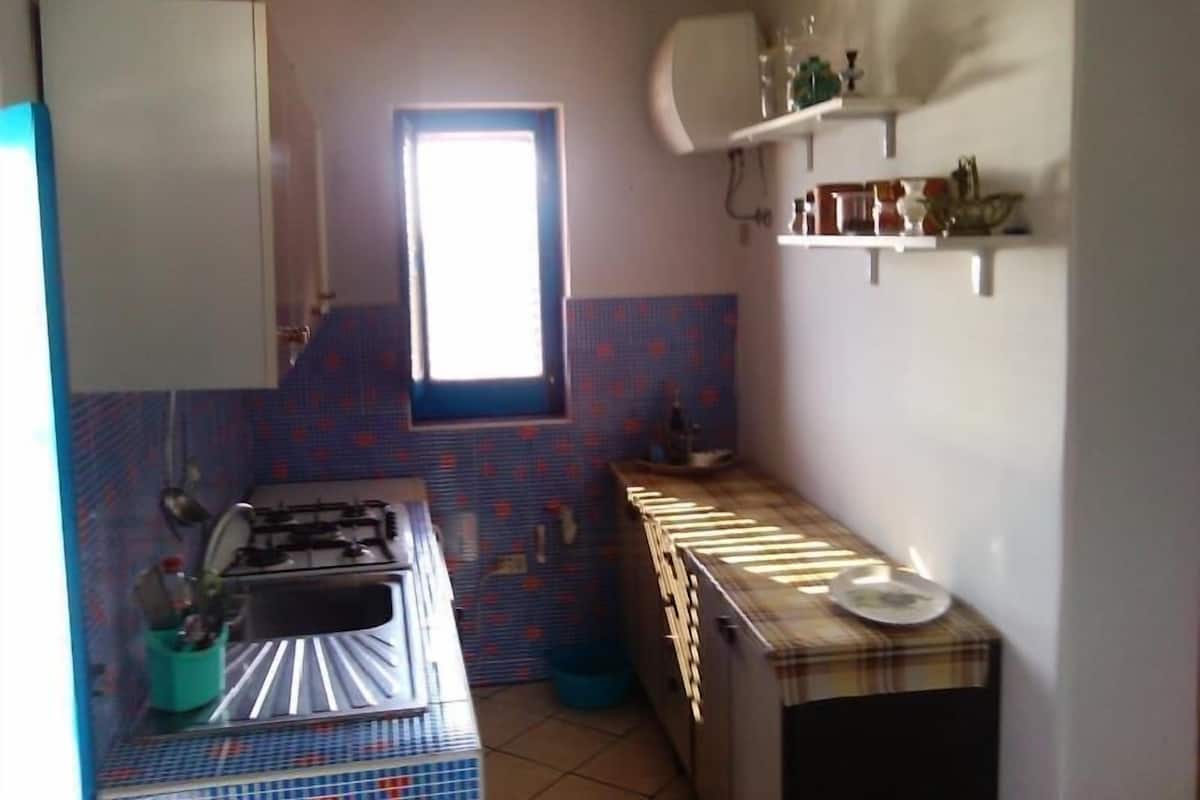 Une cuisine de taille réduite, équipée d’une cuisinière à gaz, d’une fenêtre et d’un pare-feu en carreaux.