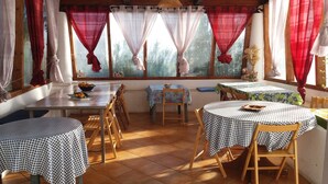 A dining area with checkered tablecloths, wooden chairs, and a window with curtains. - Case La Pergola (Santa Marina Salina)
