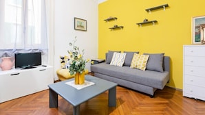 A modern living room with a sofa, a coffee table, a TV, and a yellow accent wall. - GuestHost - APT X3 Loreto Città Studi M1/M2 & C.so Buenos Aires (Milano)