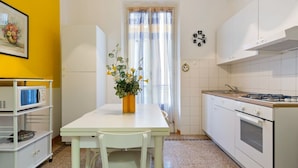A kitchen with a white table, a microwave, an oven, and a window with curtains. - GuestHost - APT X3 Loreto Città Studi M1/M2 & C.so Buenos Aires (Milano)