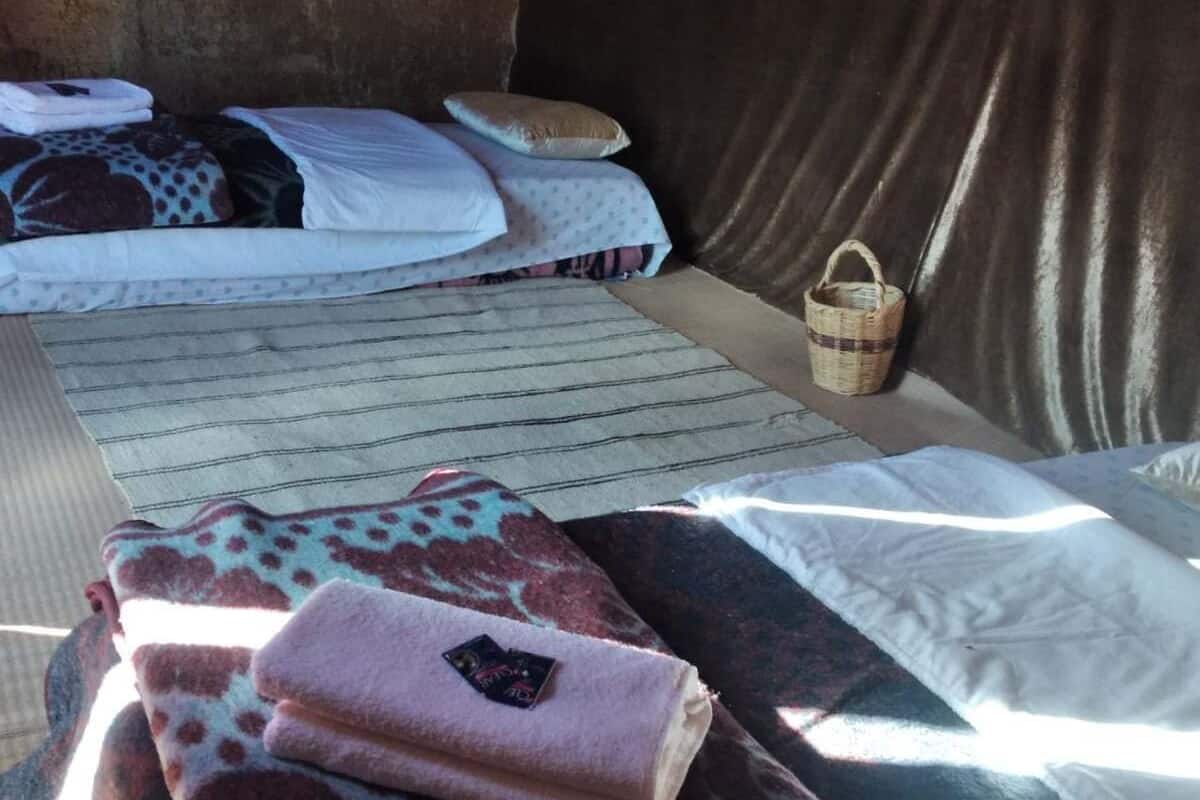 Een bed met een geboeide deken, een kussen en een opgevouwen handdoek. Er staat een mand op de vloer.