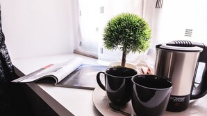 A table with two black cups, a small potted plant, a magazine, and a stainless steel coffee pot. - Roma Centrale Fidelis (Rome)