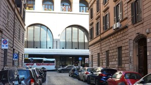 A cobblestone street lined with parked cars and motorcycles, a bus, and historic buildings with arched windows. - Roma Centrale Fidelis (Rome)