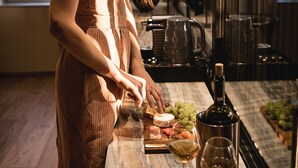 A woman in a striped dress standing by a counter with a wine bottle, glasses, and a fruit platter. - Divino Suites Chania (Chania)