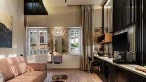 A modern living room with a sofa, coffee table, and a kitchen area with a TV and counter. - Divino Suites Chania (Chania)