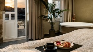 A hotel room with a large bed, a dining area with a table set for breakfast, a potted plant, and a view of the cityscape through the window. - Divino Suites Chania (Chania)