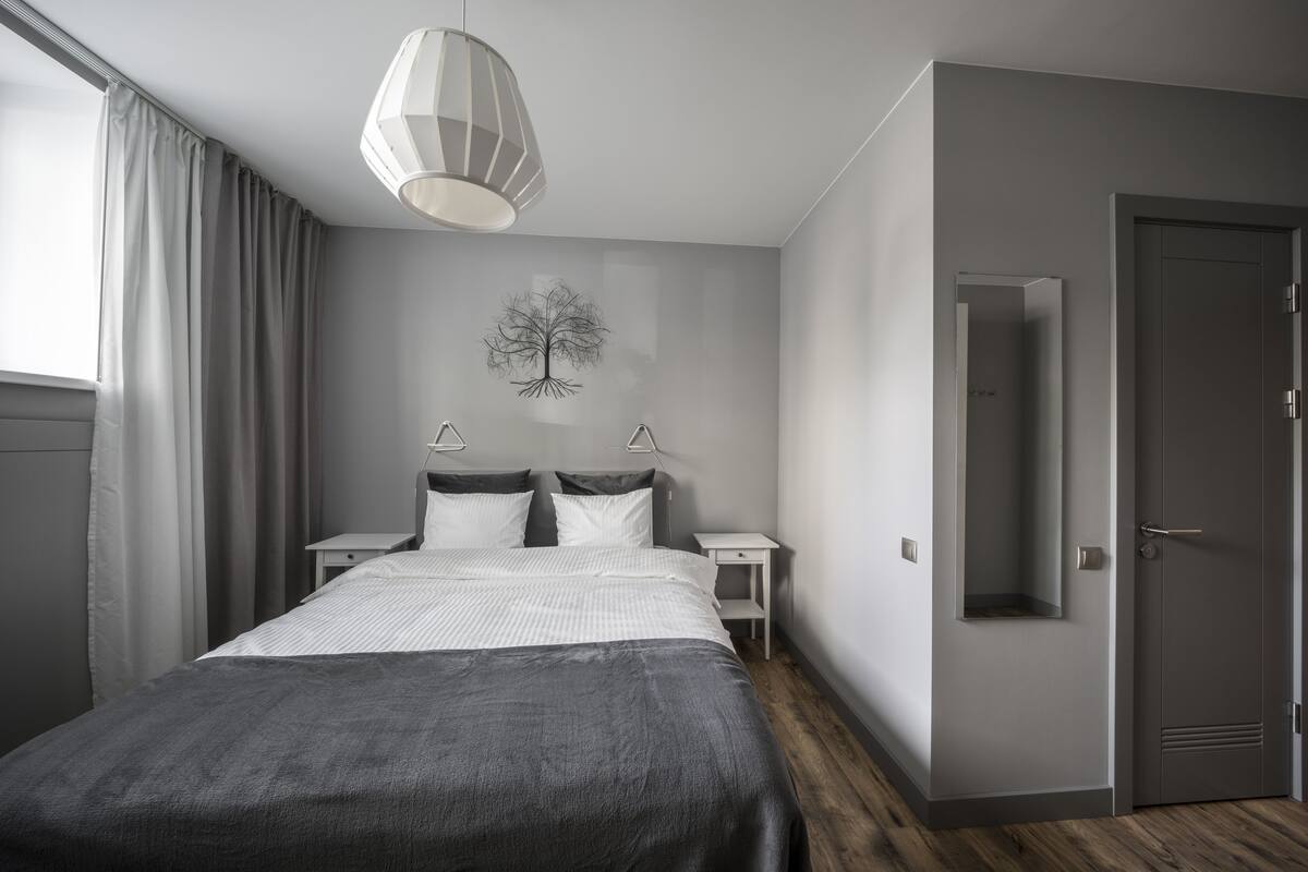 A modern bedroom with a large bed, bedside tables, a wall-mounted tree decoration, and a door with a mirror.