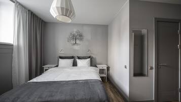 Un dormitorio moderno con una cama grande, mesitas de noche, un adorno de árbol en la pared y una puerta con espejo.