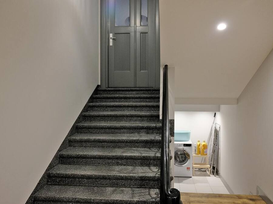 Una escalera conduce a una puerta, con una lavadora y útiles de lavandería visibles al fondo.