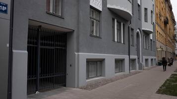 Un edificio moderno con fachada gris, entrada protegida por una reja y una acera estrecha.