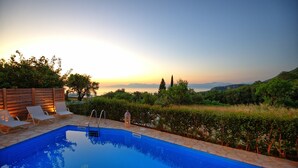 Une piscine avec des chaises longues, une clôture en bois et une vue sur la mer au coucher du soleil.