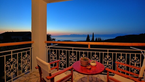 Un balcon avec une table et des chaises, offrant une vue panoramique sur les montagnes et un plan d’eau au crépuscule.