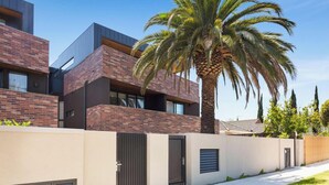 A modern building with brick and metal exterior, a palm tree, and a gated entrance. - Stylish Parkside Apartment 2 Bed 2 Bath NETFLIX  Car park 12 minutes to City (Caulfield North)