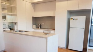 A modern kitchen with white cabinetry, a central island, a sink, and a refrigerator. - Stylish Parkside Apartment 2 Bed 2 Bath NETFLIX  Car park 12 minutes to City (Caulfield North)