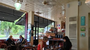A cafe with wooden tables and chairs, a counter with various items, and a view of the outdoors. - Stylish Parkside Apartment 2 Bed 2 Bath NETFLIX  Car park 12 minutes to City (Caulfield North)